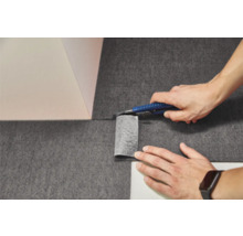 Tăierea unui material nețesut închis la culoare cu un cutter la colțul unui perete.