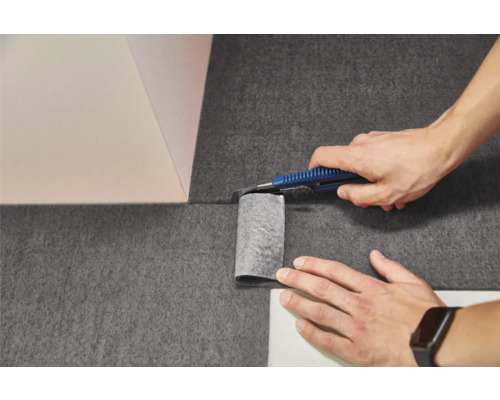 Tăierea unui material nețesut închis la culoare cu un cutter la colțul unui perete.