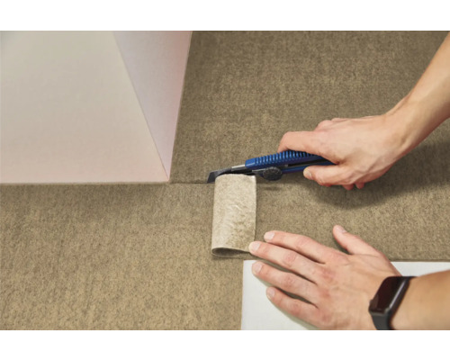 O persoană taie o pardoseală texturată din pâslă cu un cuțit utilitar.