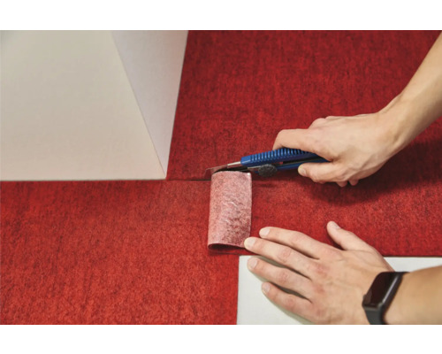 O persoană taie mocheta roșie cu un cutter.