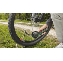 O mână ține o pompă de aer cu acumulator Bosch și umflă o anvelopă de bicicletă în aer liber.