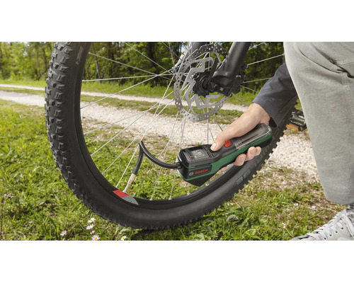 O mână ține o pompă de aer cu acumulator Bosch și umflă o anvelopă de bicicletă în aer liber.