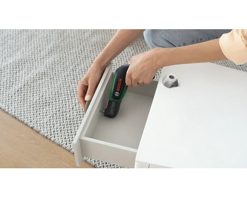 Șurubelniță cu acumulator Bosch IXO cu adaptor unghiular utilizată pentru înșurubarea unui sertar la o piesă de mobilier albă.