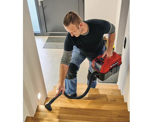 Un bărbat curăță o scară de lemn cu un aspirator compact Einhell cu acumulator pentru aspirare umedă și uscată.