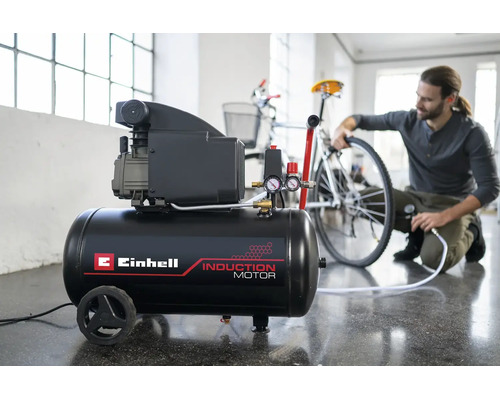 Compresor Einhell cu motor cu inducție într-un atelier luminos, un bărbat umflă o anvelopă de bicicletă.