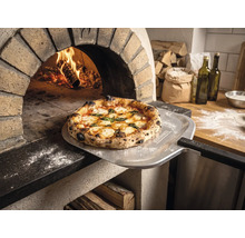 Pizza proaspăt coaptă pe o paletă pentru pizza cu Tenneker Logo în fața unui cuptor de piatră aprins într-o bucătărie rustică.
