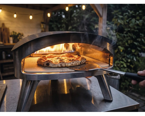 Cuptor de pizza din oțel inoxidabil pentru exterior cu flăcări și o pizza pe piatră de pizza, manevrată cu o paletă pentru pizza.