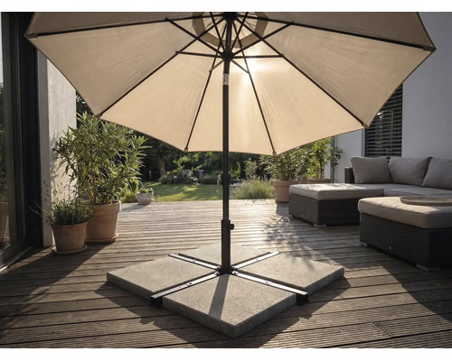Umbrelă de soare pe o terasă din lemn cu suport din plăci de beton, mobilier de grădină și plante într-un spațiu exterior luminos.