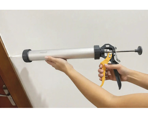 O persoană utilizează un pistol de etanșare tubular Precit pentru a etanșa un rost între perete și tocul ușii.