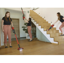 O femeie folosește un aspirator vertical roșu pentru podele, pereți și scări din lemn într-o cameră modernă și luminoasă.