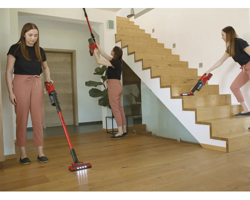 O femeie folosește un aspirator vertical roșu pentru podele, pereți și scări din lemn într-o cameră modernă și luminoasă.