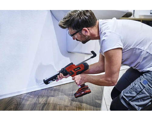 Un meșter folosește un pistol pentru cartușe cu acumulator Einhell pentru a etanșa un rost la plinta peretelui.