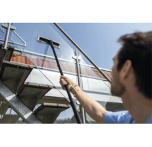 O persoană curăță o balustradă din sticlă a unei scări exterioare cu un ștergător de ferestre telescopic.