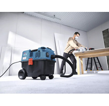 Un aspirator umed uscat Bosch conectat la un ferăstrău circular cu incizie în timp ce un meșter prelucrează o placă de lemn într un atelier luminos.
