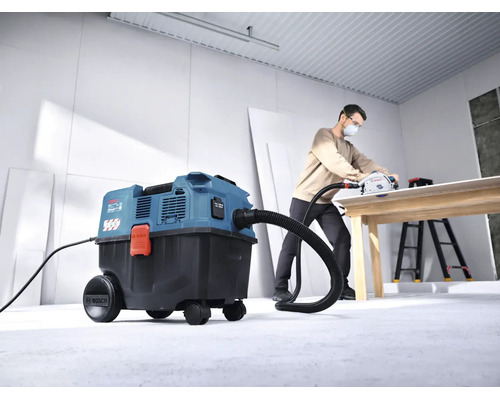 Un aspirator umed uscat Bosch conectat la un ferăstrău circular cu incizie în timp ce un meșter prelucrează o placă de lemn într un atelier luminos.