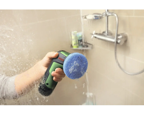 O persoană curăță o cabină de duș cu dispozitivul de curățare fără fir Bosch și un accesoriu de burete albastru.