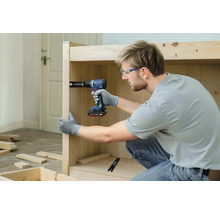 Un meșter fixează un panou de lemn pe corpul unei piese de mobilier folosind o mașină de găurit și înșurubat cu acumulator Bosch.