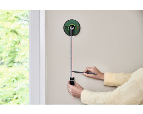 O persoană folosește un telemetru laser pentru a măsura pe un perete.