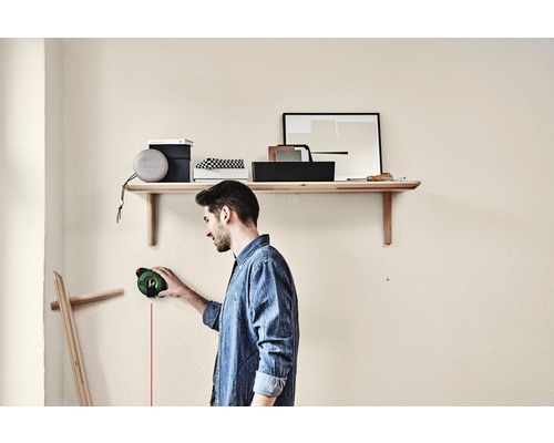 "Un bărbat folosește o laser linie pentru a alinia un suport de perete