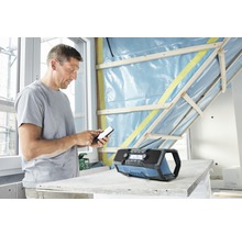 Un bărbat operează un telefon mobil lângă un radio de șantier într-o cameră cu pereți neterminați