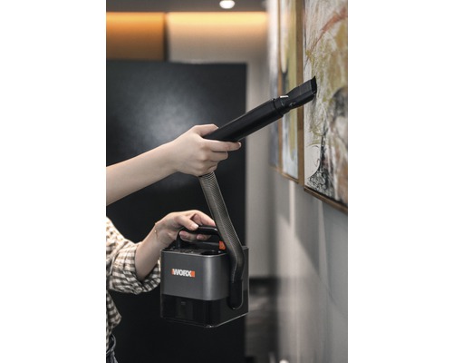 O persoană curăță un tablou de pe perete cu un aspirator portabil Worx.