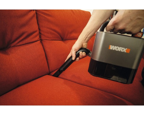 O persoană aspiră o canapea cu un aspirator fără fir Worx