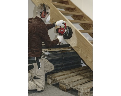 Un meșter șlefuiește o scară din lemn cu o freză de canelat pereți și poartă echipament de protecție.