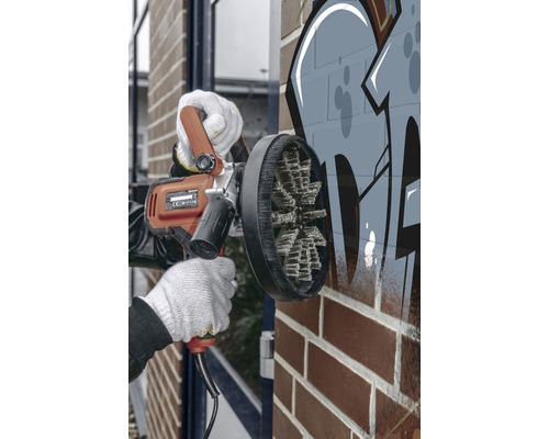 O persoană folosește o mașină de îndepărtat graffiti de pe un zid de cărămidă.