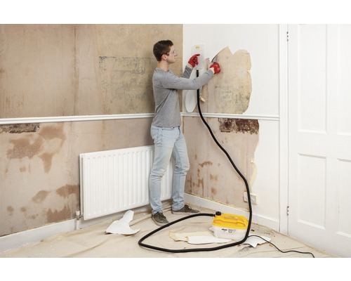 Un bărbat îndepărtează tapetul cu un aparat de îndepărtat tapetul într-o cameră.