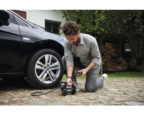 Bărbat umflând o anvelopă de mașină cu un compresor cu acumulator