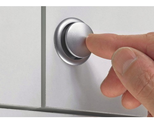 Un deget apasă un buton de mobilier argintiu pe o suprafață albă