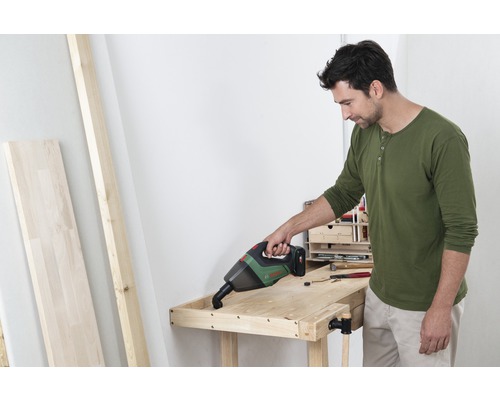 Un bărbat aspiră un banc de lucru din lemn cu un aspirator portabil fără fir.