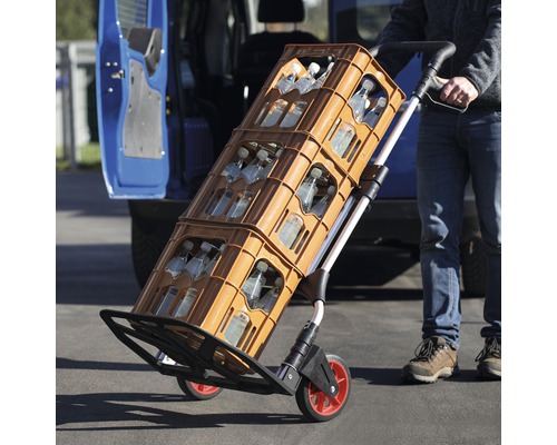 Un cărucior transportă lăzi cu băuturi în fața unui vehicul.