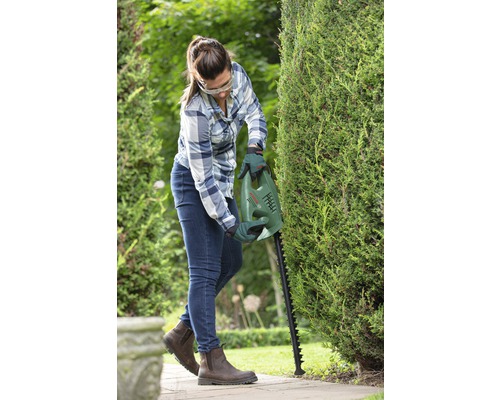 Femeie taie un gard viu cu o foarfecă de tuns gardul viu Bosch în grădină.