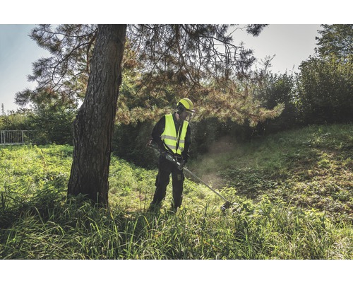 Un bărbat în echipament de protecție lucrează cu o mașină de tuns iarba în aer liber.