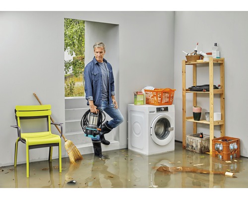 Bărbat cu pompă submersibilă într-o pivniță inundată cu mașină de spălat și raft