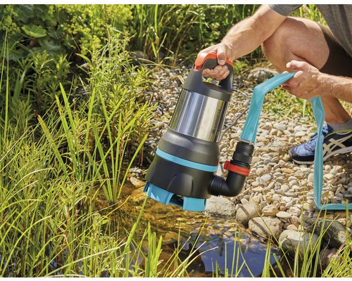 O persoană ține o pompă submersibilă pentru ape murdare Gardena cu un furtun conectat deasupra unui iaz