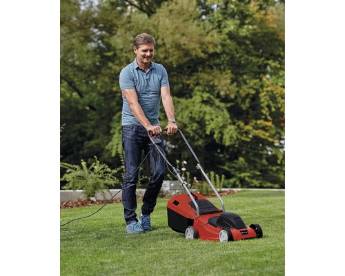 Bărbat tunde gazonul cu o mașină de tuns iarba electrică roșie în grădină.