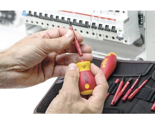 Bărbat schimbând un bit de șurubelniță Wiha în fața unei cutii de distribuție