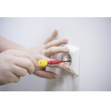 O mână efectuează lucrări electrice cu o șurubelniță la o priză.