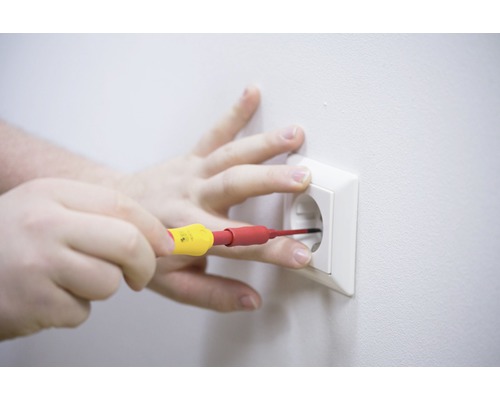 O mână efectuează lucrări electrice cu o șurubelniță la o priză.