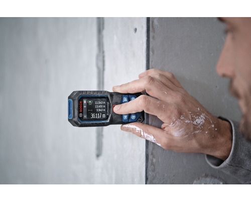 O persoană folosește un telemetru Bosch pe un perete pentru a măsura.