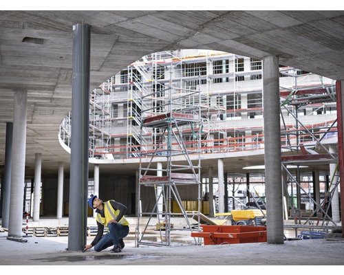 Muncitor în construcții măsurând o coloană de oțel pe un șantier.