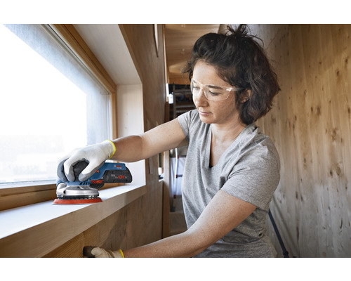 Femeie șlefuind un toc de fereastră cu o șlefuitoare excentrică