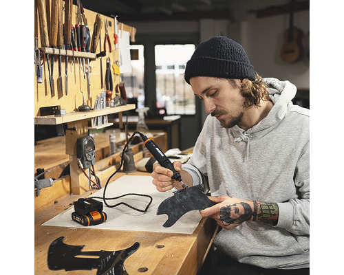 Bărbat lucrând cu un instrument multifuncțional pe o piesă de lucru pe un banc de lucru.