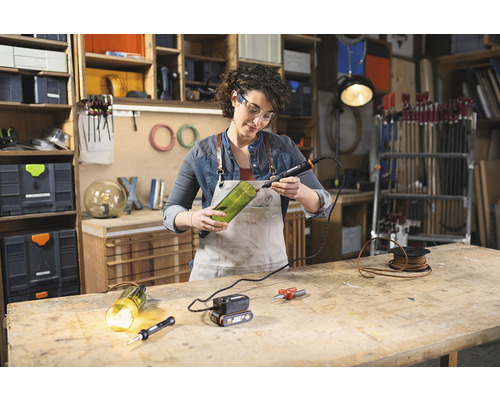 Femeie găurind o sticlă de sticlă cu o unealtă rotativă pentru proiecte de bricolaj într-un atelier.