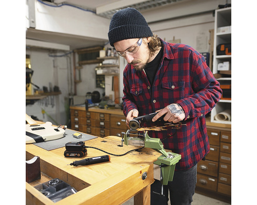 Bărbat lucrând cu un polizor unghiular pe o piesă fixată într-o menghină pe un banc de lucru. Se mai vede și un instrument multifuncțional și o baterie.