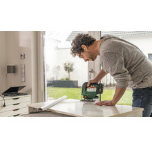 Un bărbat taie o piesă cu un fierăstrău vertical. Poartă ochelari de protecție și protecție auditivă.