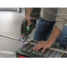 O persoană taie o țeavă cu un ferăstrău pendular fără fir pe o masă de tăiat.