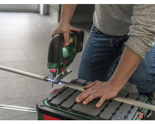 O persoană taie o țeavă cu un ferăstrău pendular fără fir pe o masă de tăiat.